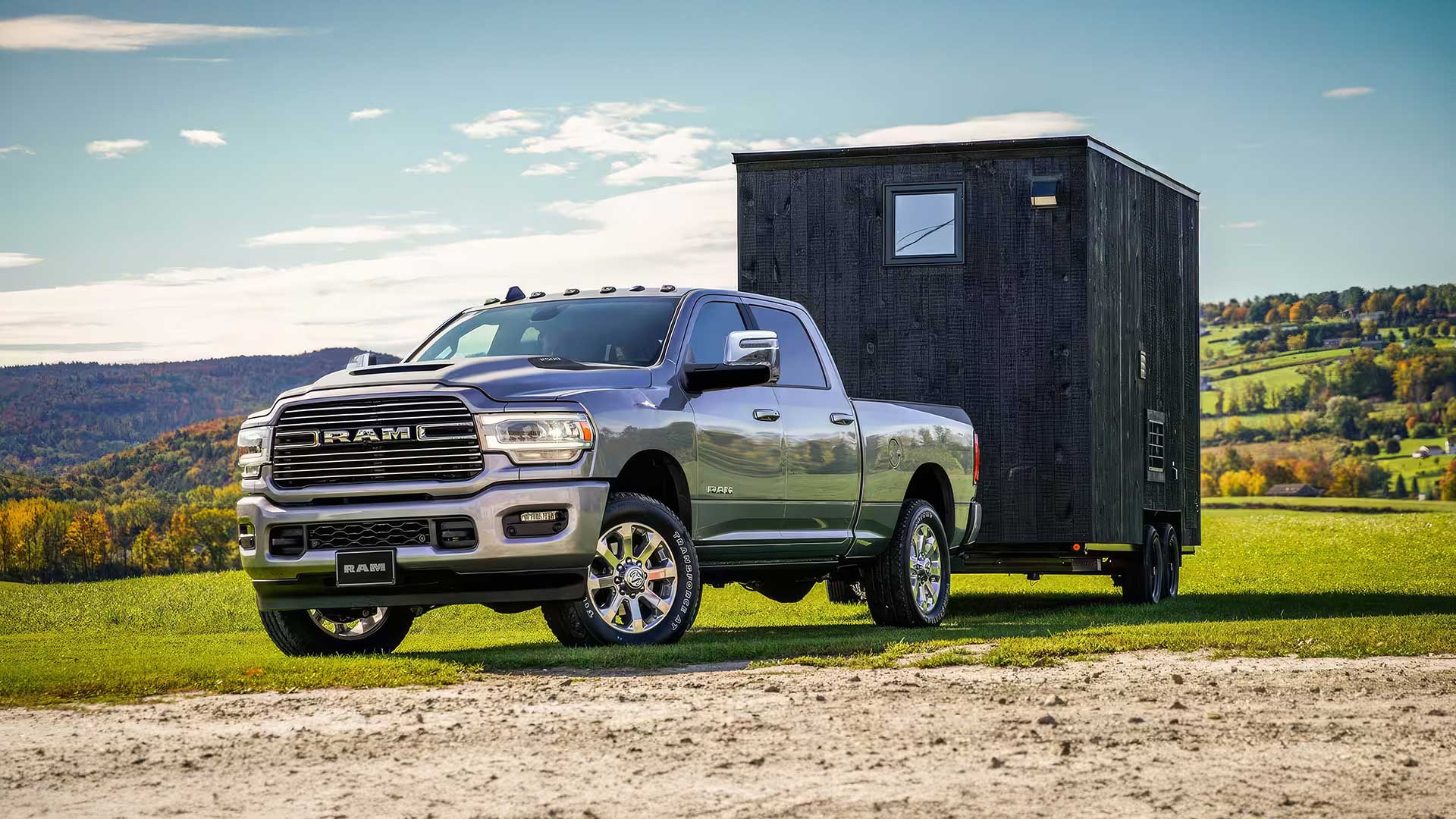 silver dodge ram 2500 heavy duty truck towing black trailer on grassy hillside in autumn landscape